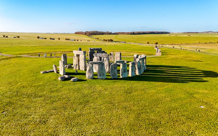 Stonehenge stone circle on a sunny day with green fields, viewed from above.