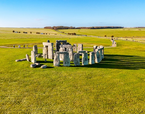 Stonehenge stone circle on a sunny day with green fields, viewed from above.