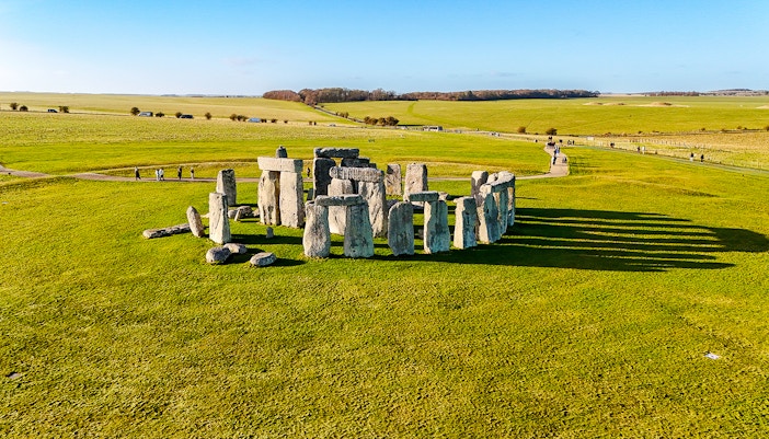Stonehenge stone circle on a sunny day with green fields, viewed from above.