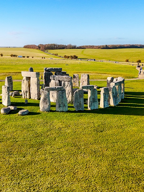 Stonehenge stone circle on a sunny day with green fields, viewed from above.