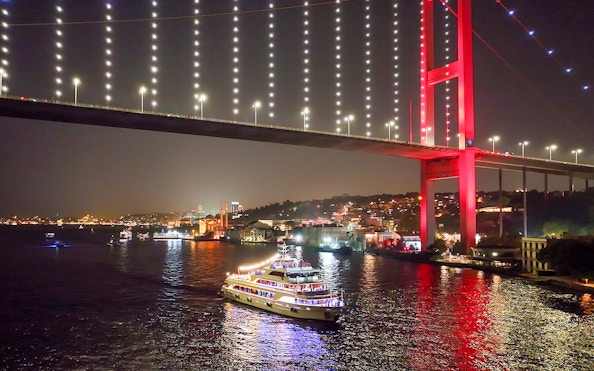Bosphorus dinner cruise ship under illuminated bridge at night in Istanbul.