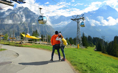 Couple admiring Grindelwald First cable cars with Swiss Alps backdrop in Interlaken.