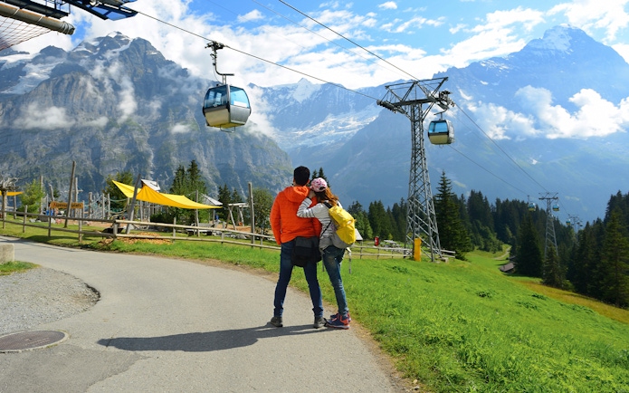 Couple admiring Grindelwald First cable cars with Swiss Alps backdrop in Interlaken.