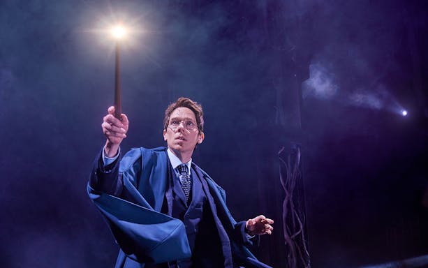 Actor holding a glowing wand in a scene from "Harry Potter and the Cursed Child" play.