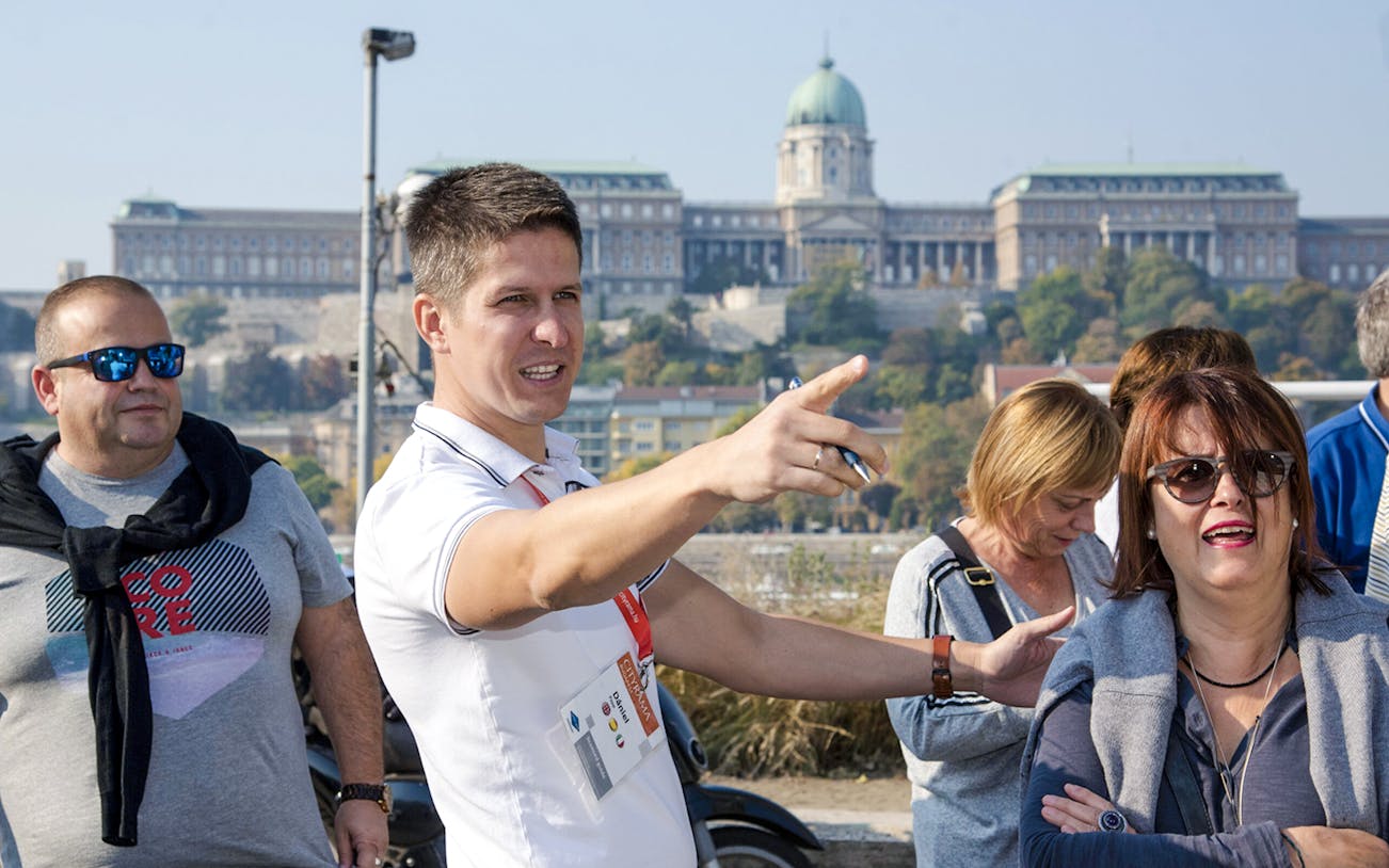 Tour guide directing guests during a Budapest walking tour with Buda Castle in the background.