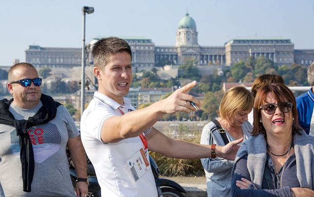 Tour guide directing guests during a Budapest walking tour with Buda Castle in the background.