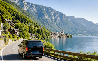 Van driving along a lakeside road towards Hallstatt village with mountains in the background.