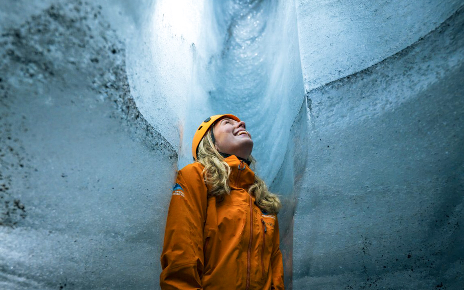 Guest inside Katla Ice Cave wearing helmet and jacket, admiring icy walls.