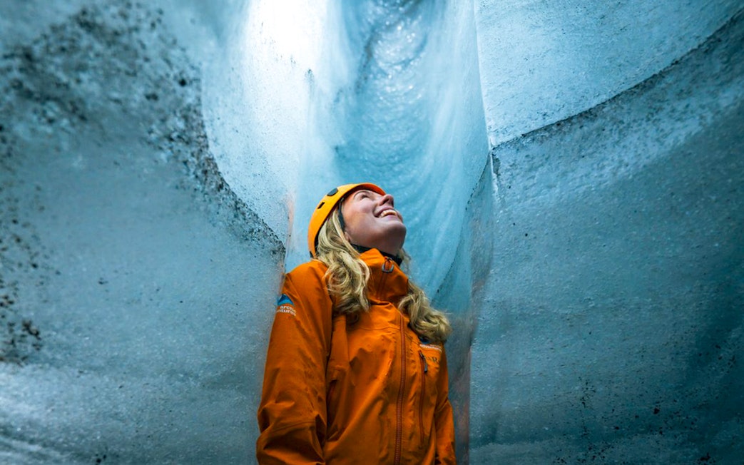 Guest inside Katla Ice Cave wearing helmet and jacket, admiring icy walls.
