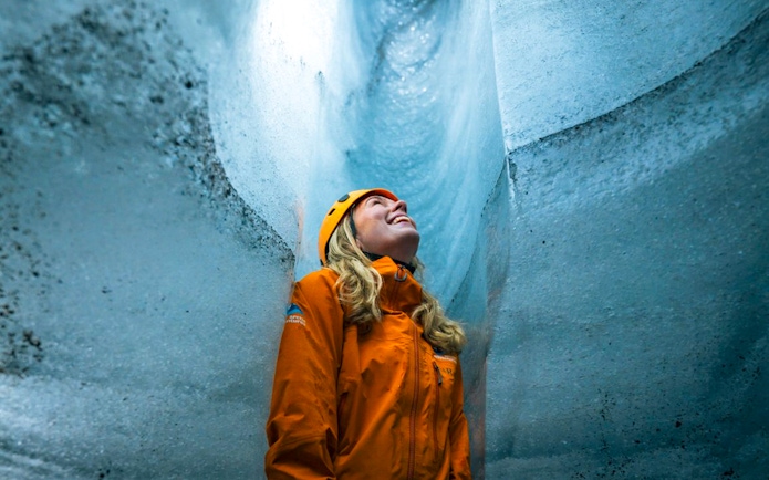 Guest inside Katla Ice Cave wearing helmet and jacket, admiring icy walls.