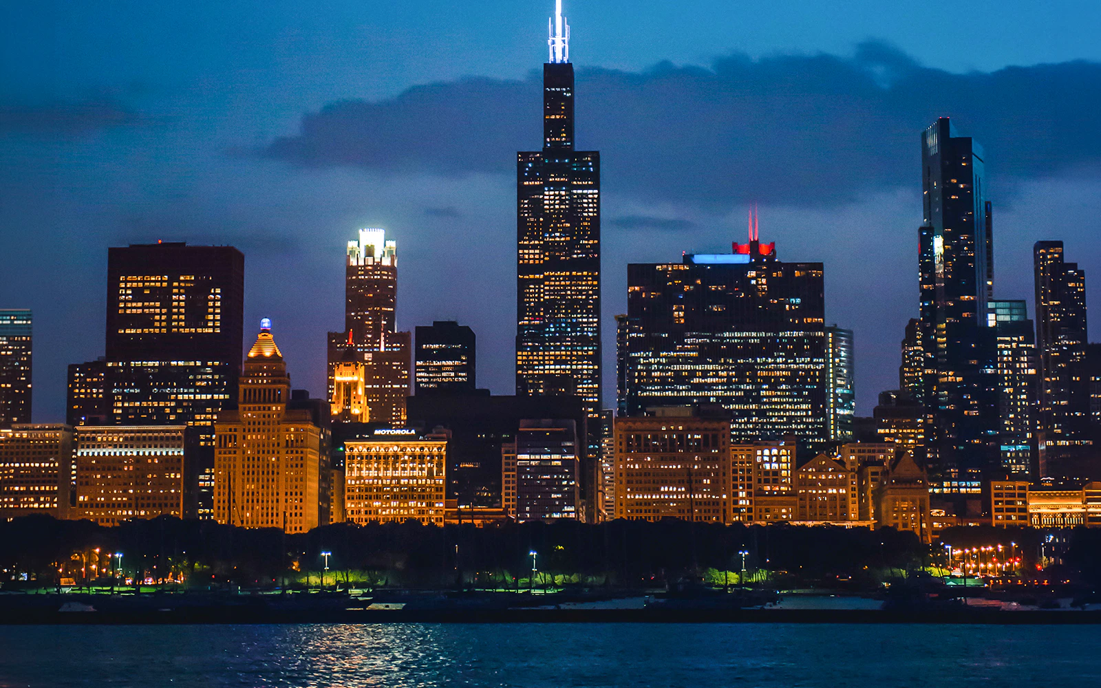 Chicago skyline at night viewed from a river cruise, featuring illuminated skyscrapers.