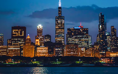 Chicago skyline at night viewed from a river cruise, featuring illuminated skyscrapers.