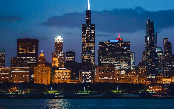 Chicago skyline at night viewed from a river cruise, featuring illuminated skyscrapers.