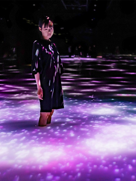 Person standing in illuminated water at teamLab Planets Tokyo exhibit.