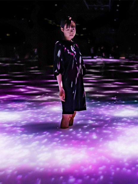 Person standing in illuminated water at teamLab Planets Tokyo exhibit.