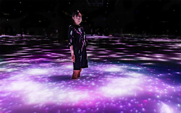 Person standing in illuminated water at teamLab Planets Tokyo exhibit.