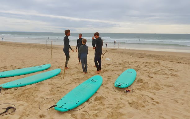 Instructor leading surf class on Lisbon beach with tourists and surfboards.