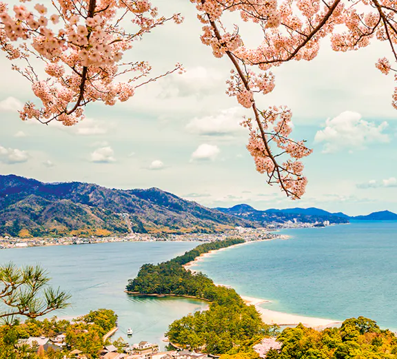 Cherry blossoms framing Amanohashidate sandbar and Miyama Kayabuki No Sato village, Japan.