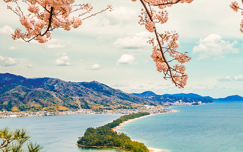 Cherry blossoms framing Amanohashidate sandbar and Miyama Kayabuki No Sato village, Japan.