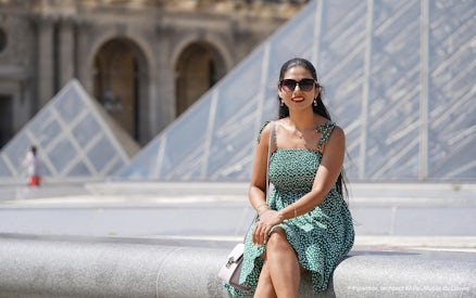 Woman sitting in front of the Louvre Pyramid during a professional photoshoot in Paris.