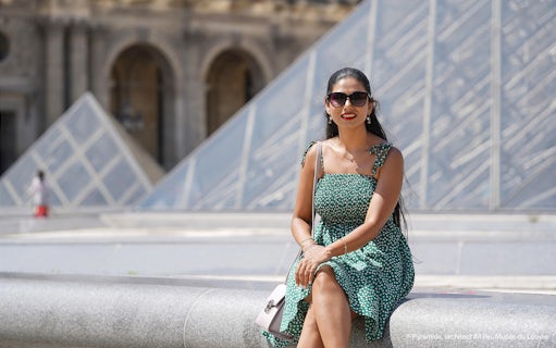Woman sitting in front of the Louvre Pyramid during a professional photoshoot in Paris.