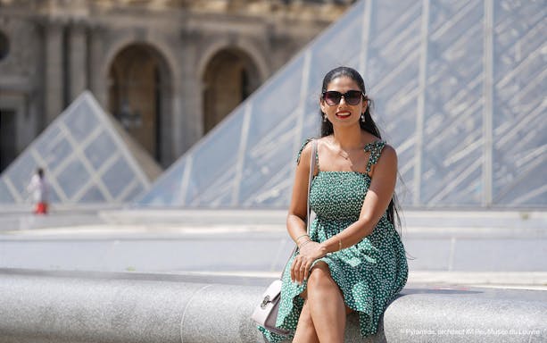 Woman sitting in front of the Louvre Pyramid during a professional photoshoot in Paris.
