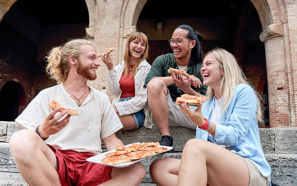 Friends enjoying pizza together on stone steps near historic arches.