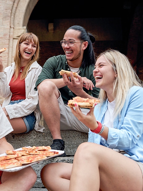 Friends enjoying pizza together on stone steps near historic arches.