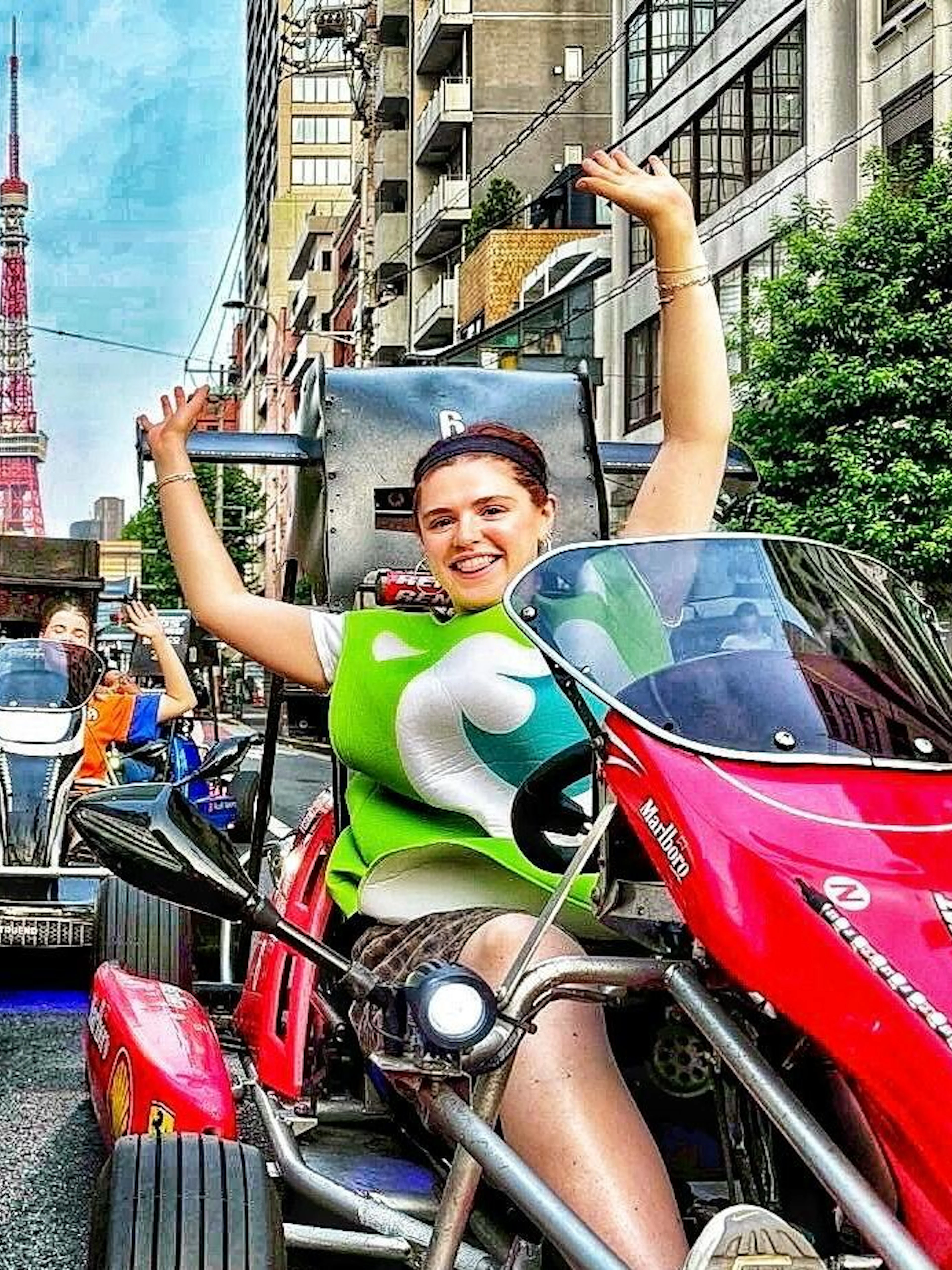 Go-kart riders in costume on Tokyo street with Tokyo Tower in background.