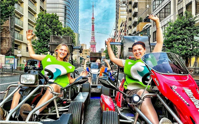 Go-kart riders in costume on Tokyo street with Tokyo Tower in background.