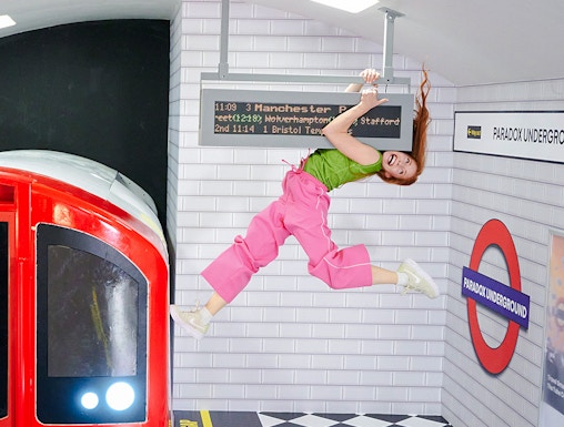 Guest hanging from a sign in a tilted subway illusion at Paradox Museum London.