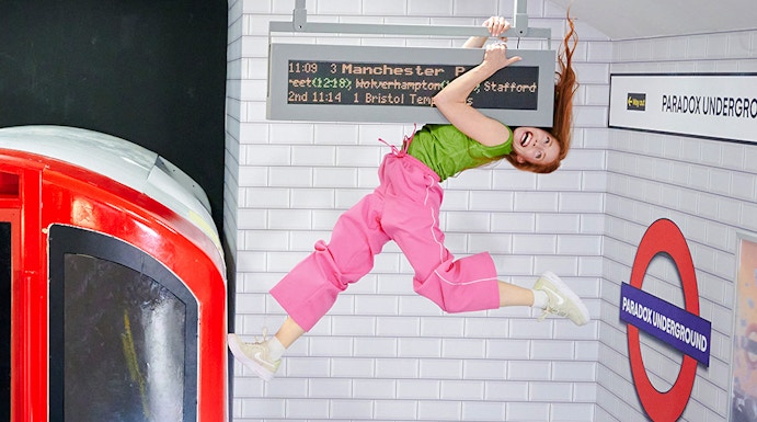 Guest hanging from a sign in a tilted subway illusion at Paradox Museum London.