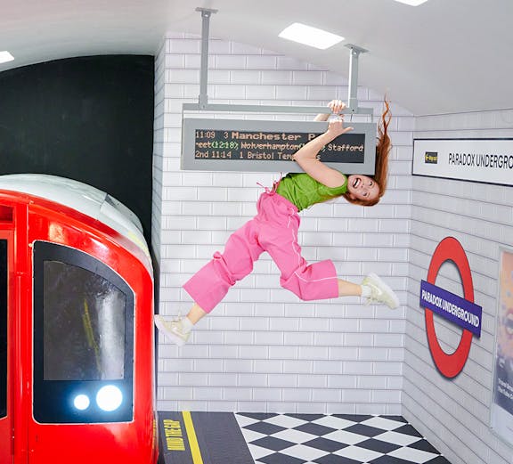 Guest hanging from a sign in a tilted subway illusion at Paradox Museum London.