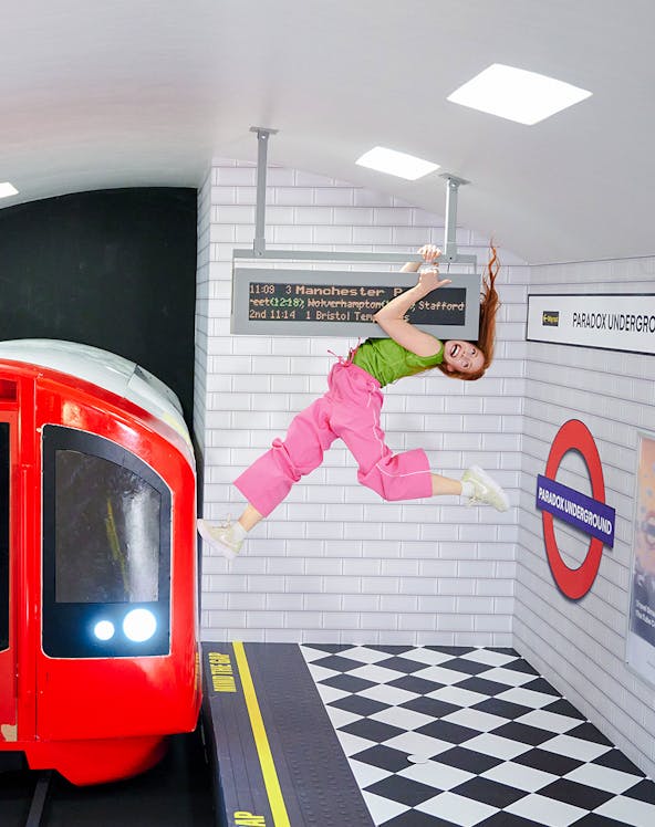 Guest hanging from a sign in a tilted subway illusion at Paradox Museum London.