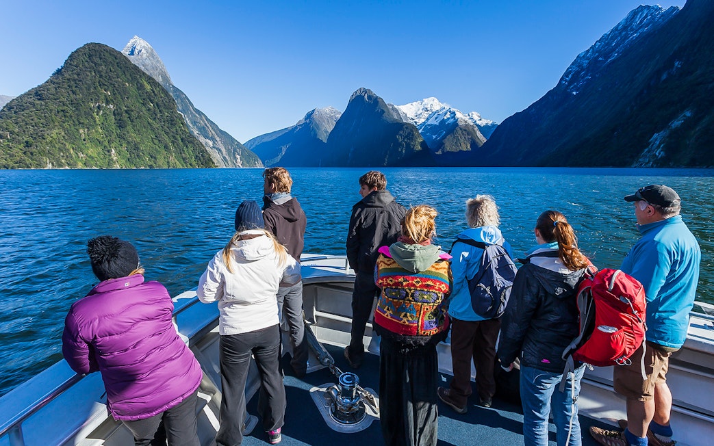 Tourists on a cruise at Milford Sound, viewing the fjord's towering cliffs and clear waters.