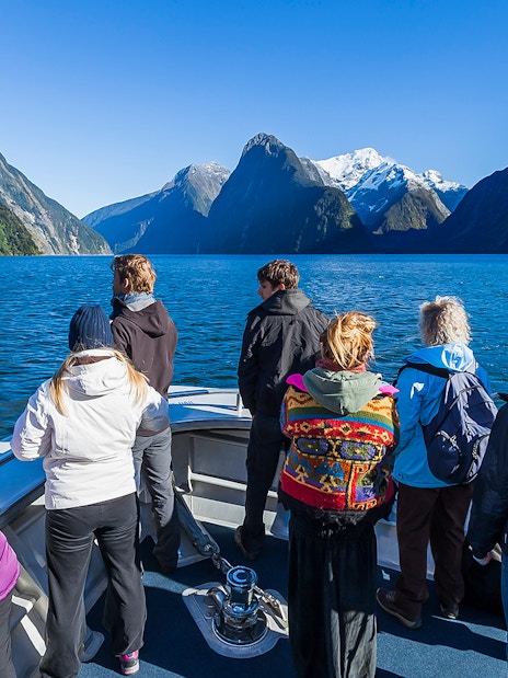 Tourists on a cruise at Milford Sound, viewing the fjord's towering cliffs and clear waters.