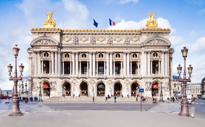 Palais Garnier facade with ornate sculptures and French flags, Paris.