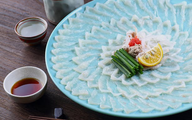 Sliced tiger puffer fish arranged on a plate with lemon, green onions, and dipping sauce at Torafugu-tei Ginza.