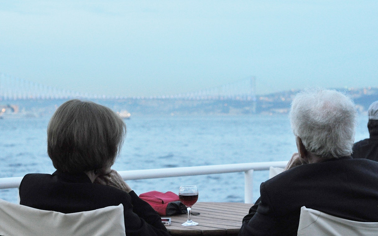 Couple enjoying Bosphorus Strait cruise with view of bridge and wine on table.