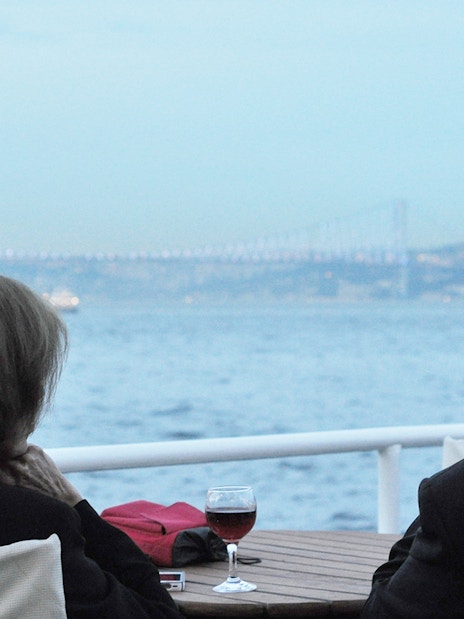 Couple enjoying Bosphorus Strait cruise with view of bridge and wine on table.