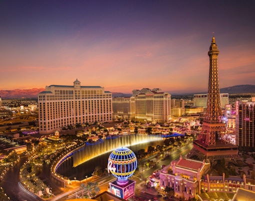 Las Vegas skyline with Bellagio fountains and Eiffel Tower replica at dusk.