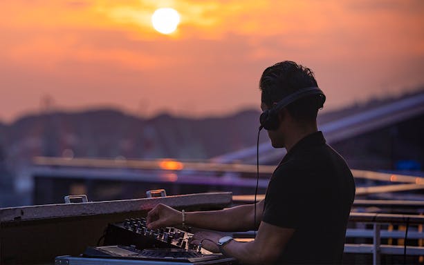 DJ playing music on a boat at sunset during Athens Riviera night party.