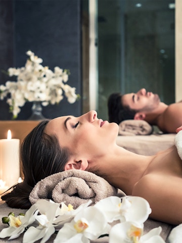 Young couple relaxing on massage beds at Asian luxury spa with orchids and candles.