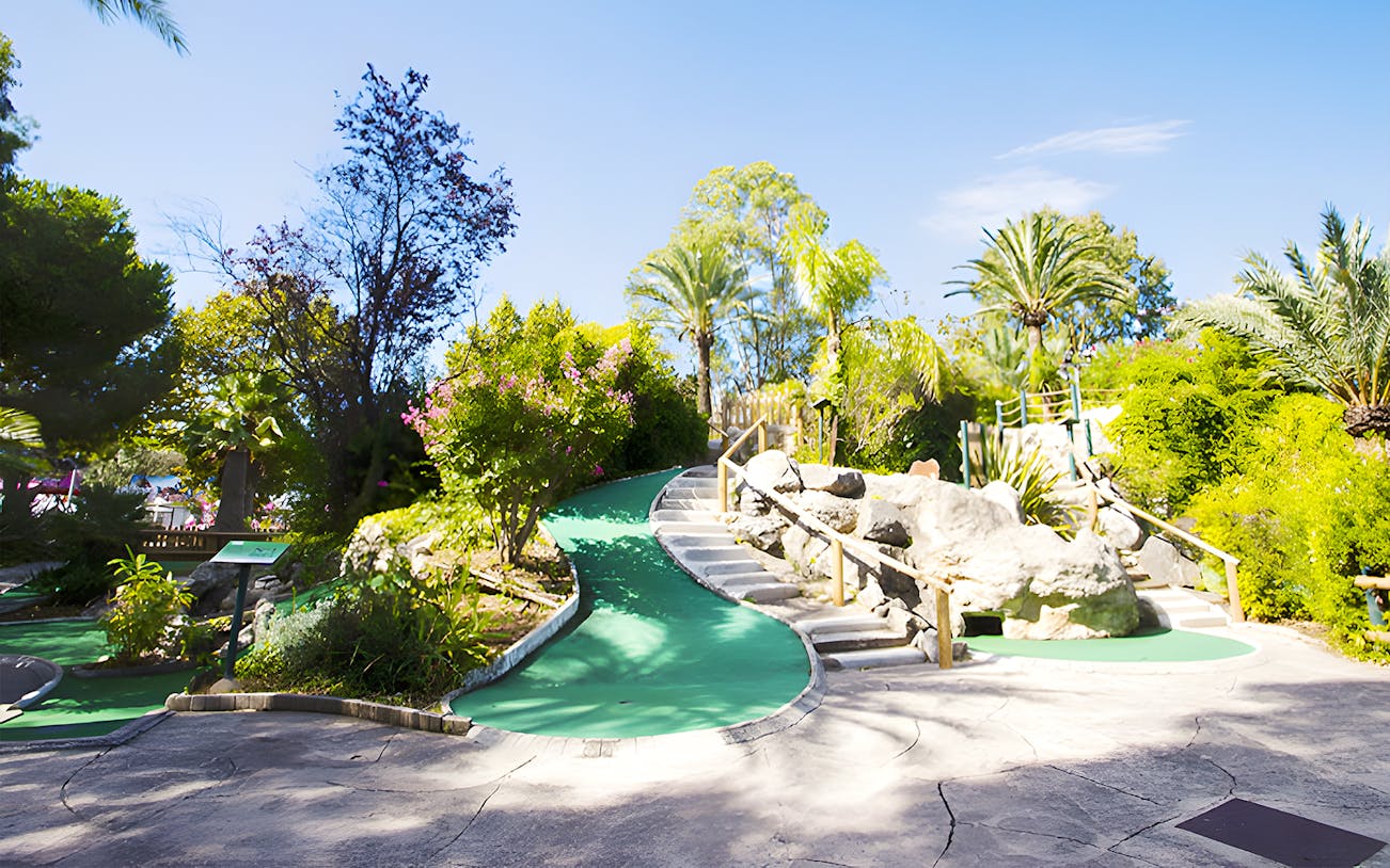 Mini-golf course with lush greenery and rock formations under a clear blue sky.