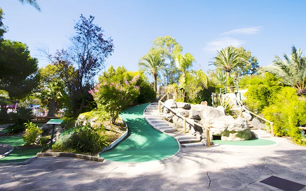 Mini-golf course with lush greenery and rock formations under a clear blue sky.