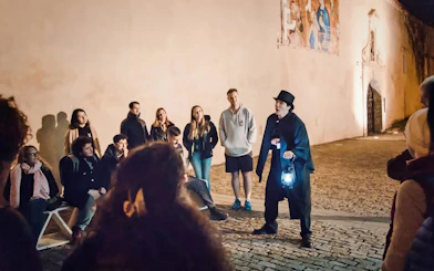 Tour guide with lantern leading Ghosts & Legends of Old Town Prague tour at night.