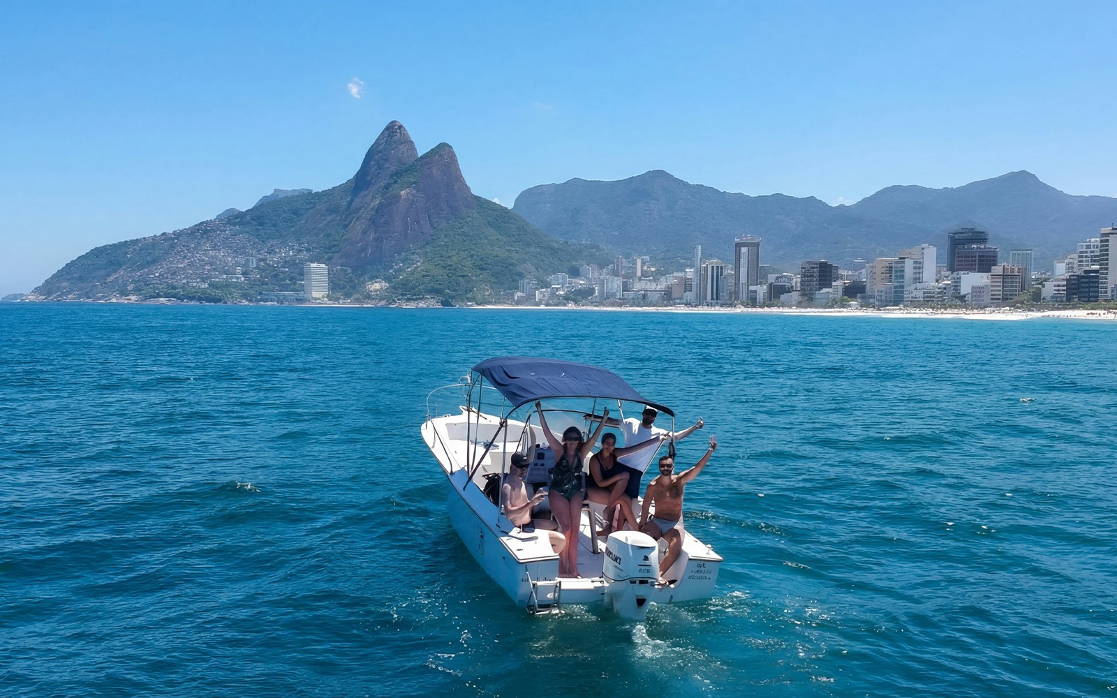 Tourists on a cruise boat with Rio de Janeiro skyline and mountains in the background.