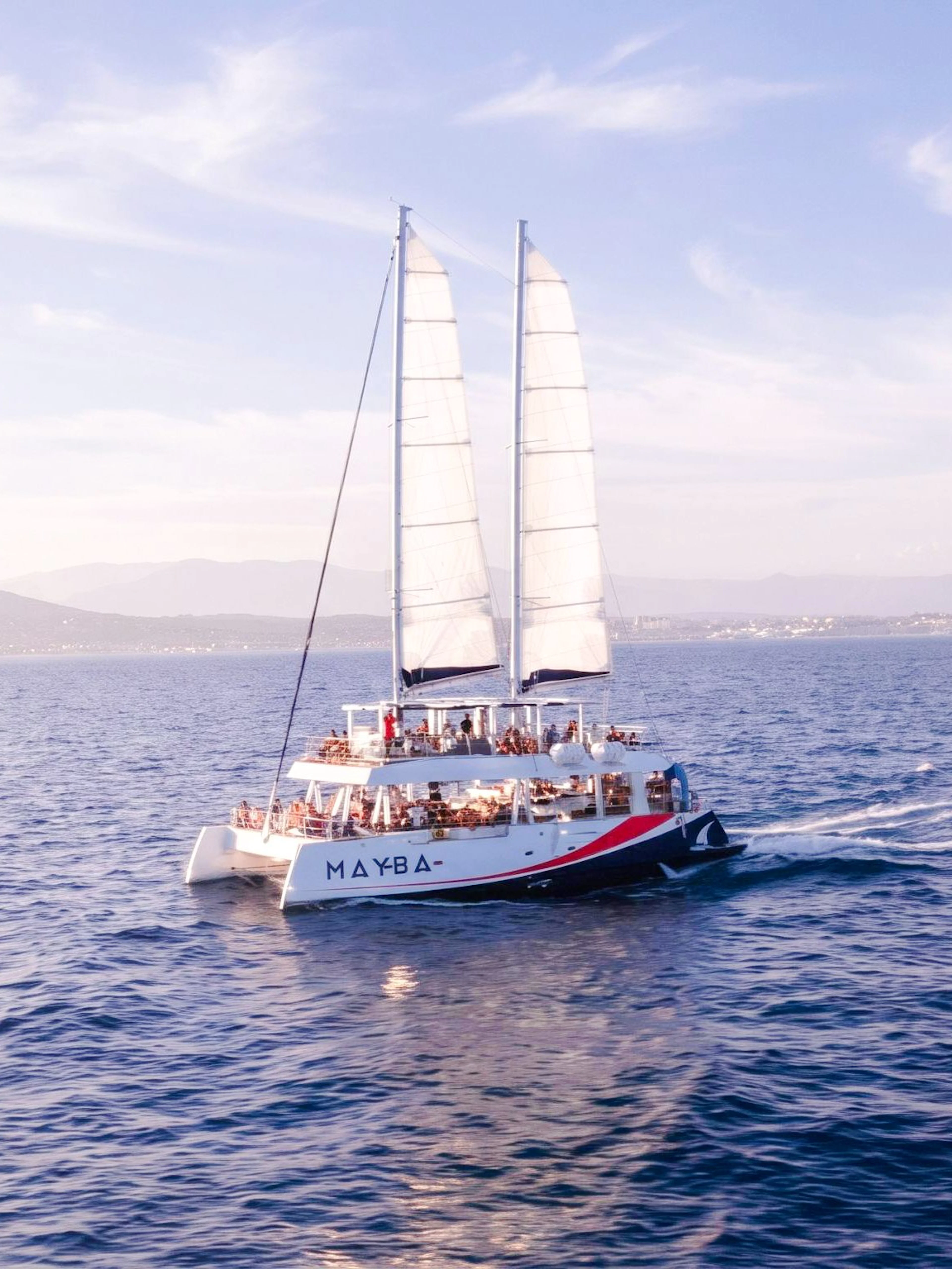 Catamaran sailing at sunset with passengers enjoying apéritifs on the open sea.