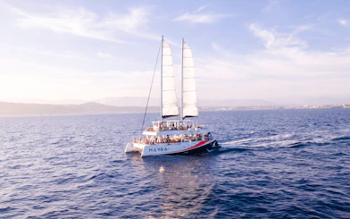 Catamaran sailing at sunset with passengers enjoying apéritifs on the open sea.