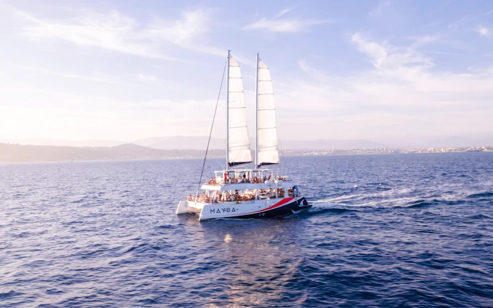 Catamaran sailing at sunset with passengers enjoying apéritifs on the open sea.